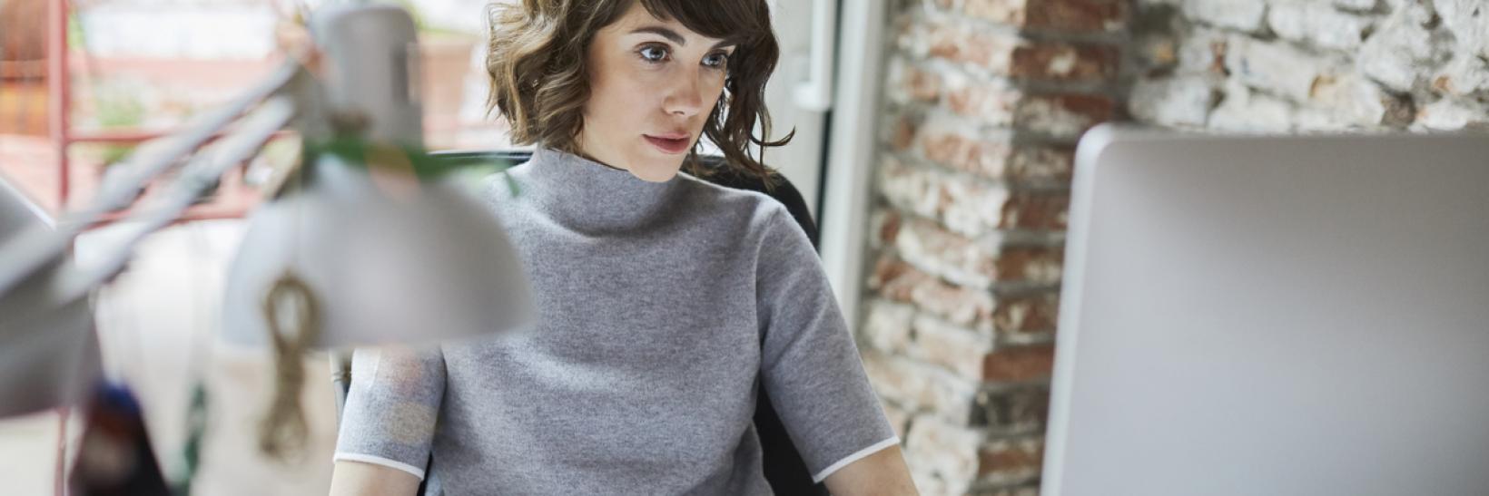 Woman sits at a computer at a desk and uses the new Frequently Asked Questions tool