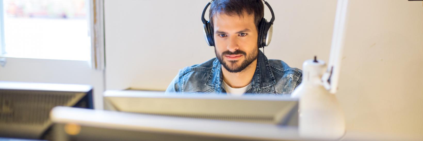 A stakeholder sits at a computer and listens to the Government Voices Webinar recording on headphones