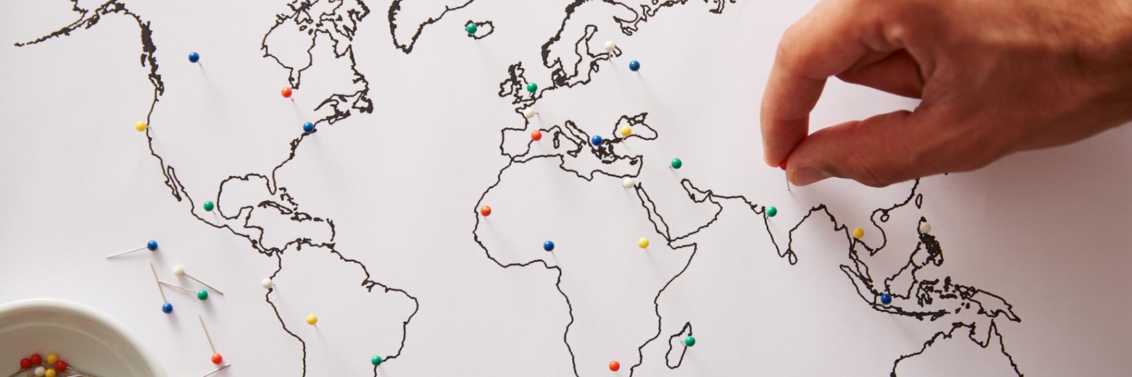 A hand adds push pins to different places on a world map