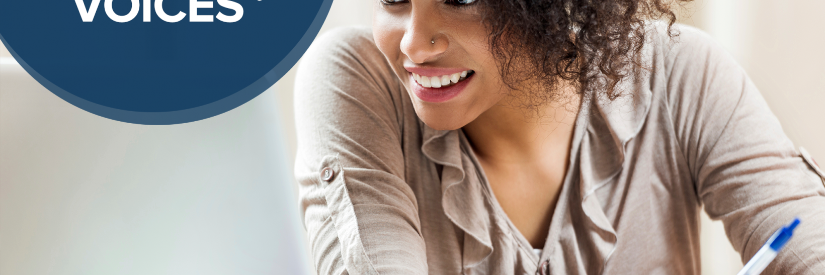 Young woman smiling and taking notes from a computer screen. Community Voices header upper left hand corner