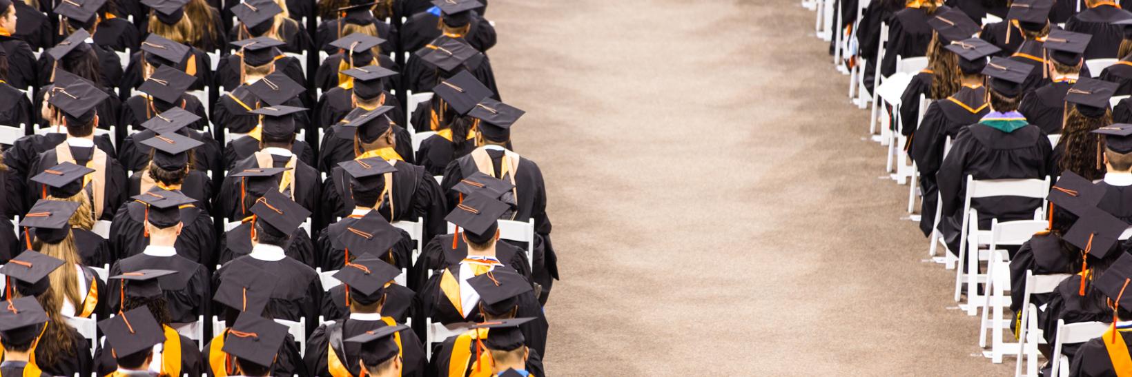 Room with rows of chairs and students sitting wearing black graduation caps and gowns