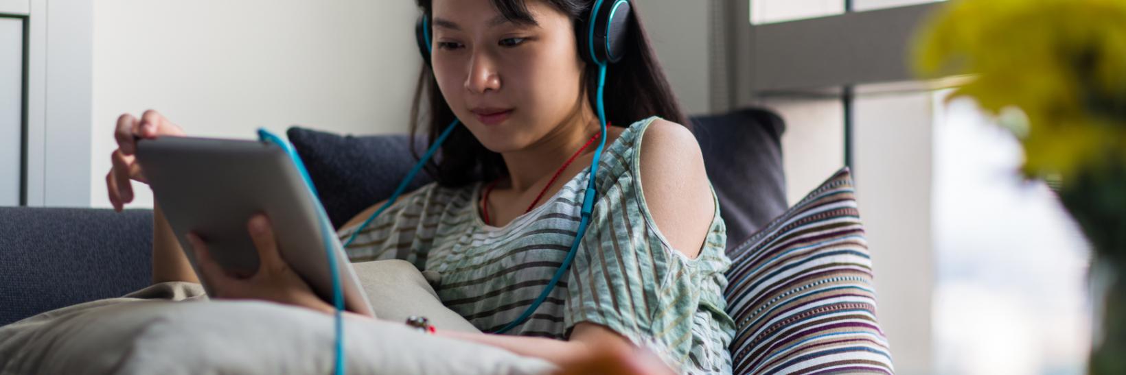 A woman with headphones on her iPad.