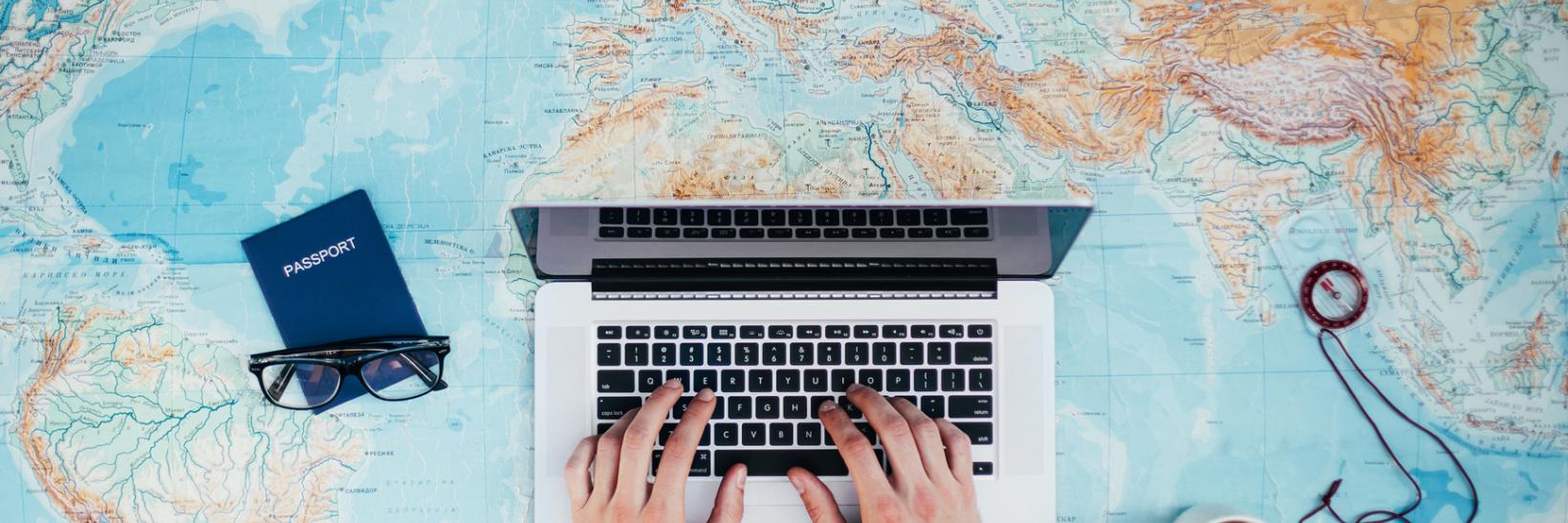 aerial point-of-view of a man typing on a laptop placed on a large world map.