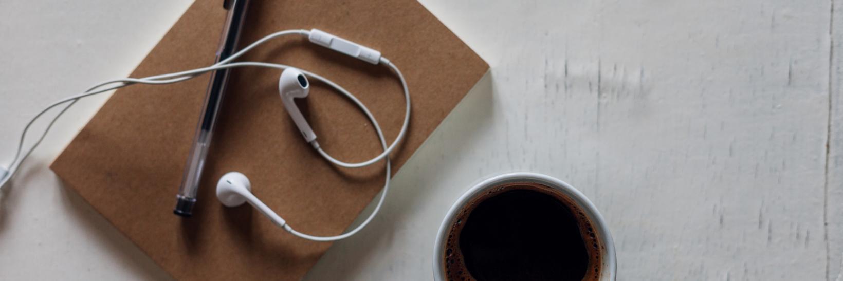 Coffee, a notepad, earphones and a pencil lying on an office desk.