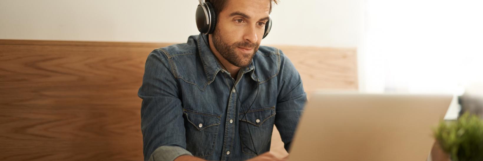 A man working on his computer and wearing headphones.