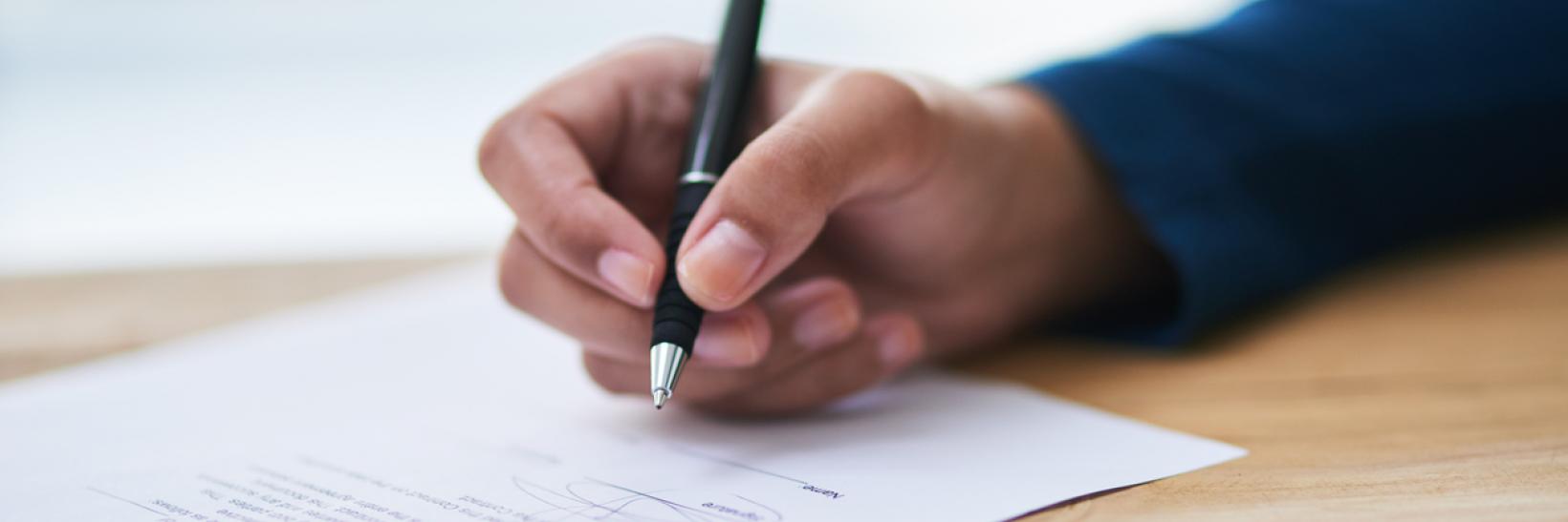 A hand writing on a piece of paper with a pen.