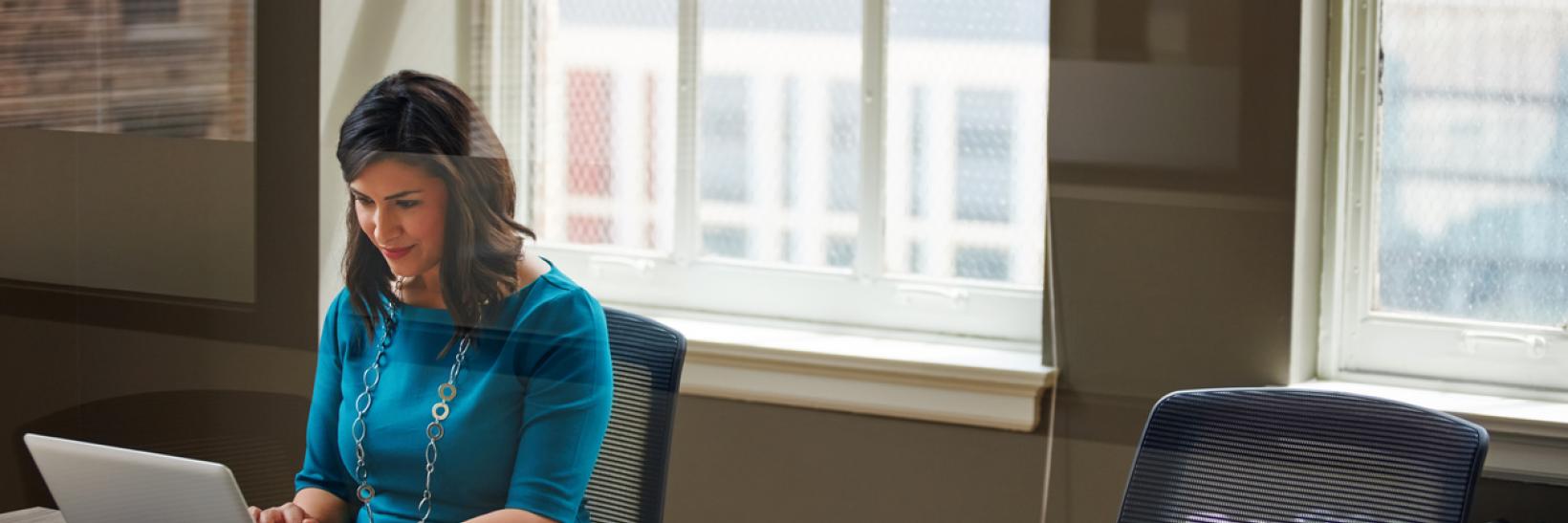 Woman sits and uses a laptop at a conference room table