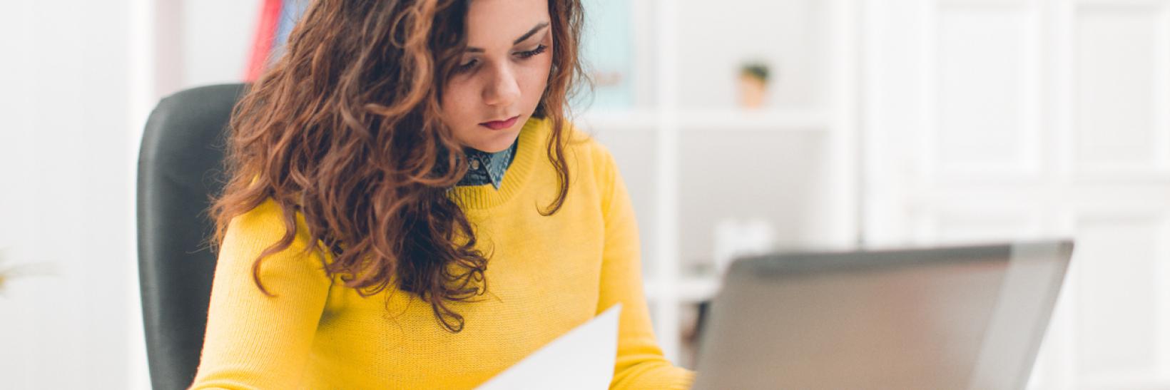 Businesswoman holding document and using laptop.