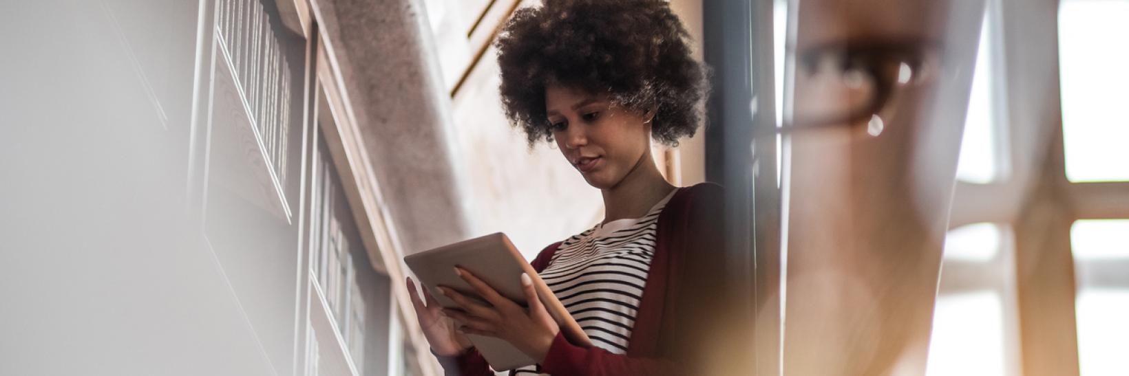 Young woman in the library standing beside the bookshelf and studying.