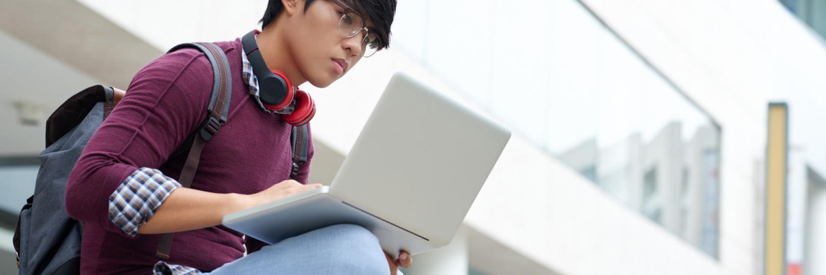 An international student working on his laptop outisde