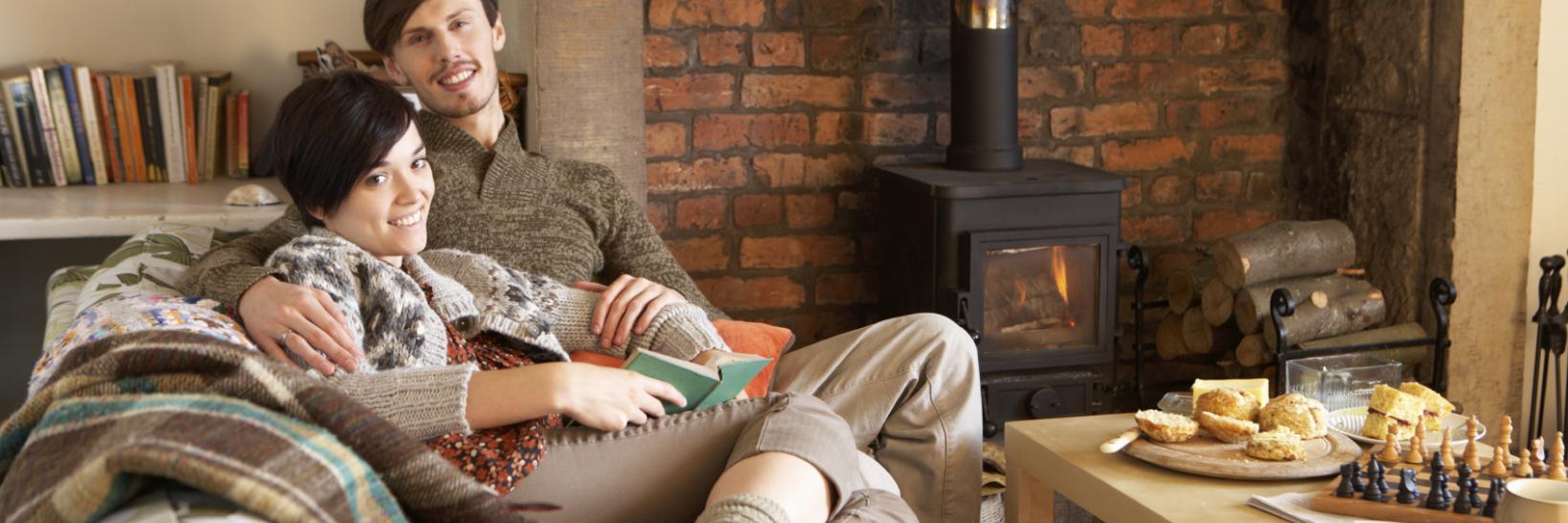 Man and woman sitting on a couch in front of a wood-burning stove