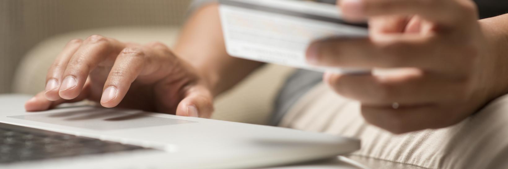 Close up of hands holding credit card in front of a laptop 