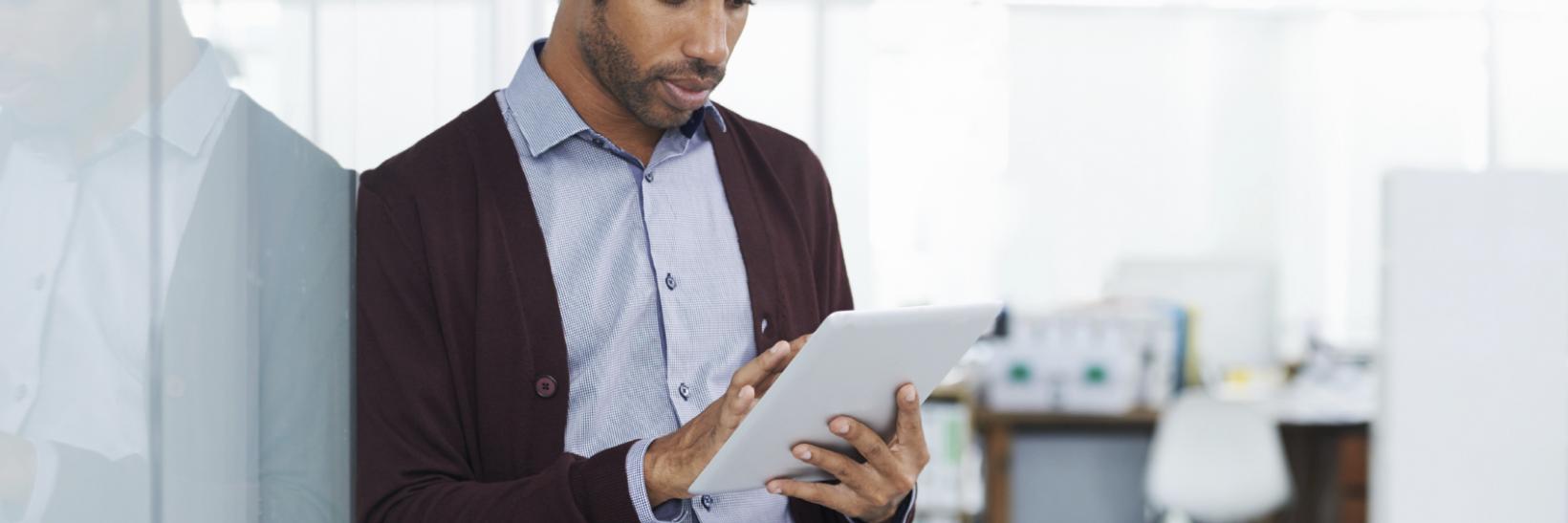 man leaning against a wall reading a tablet.