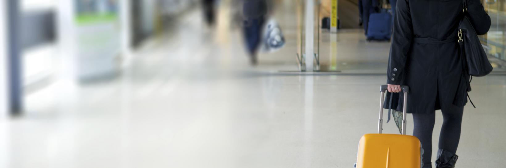 Woman walking in an airport with a roller bag suitcase 