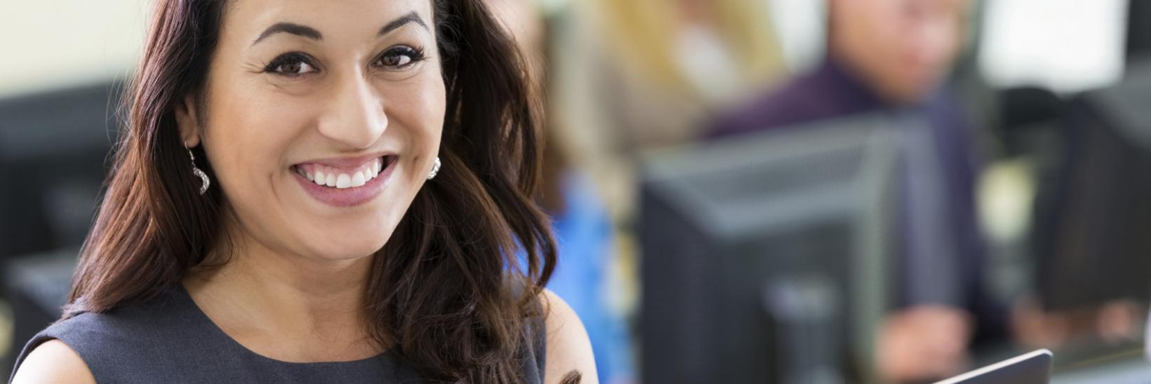 Young Latina woman sitting at a computer, smiling at the camera. 