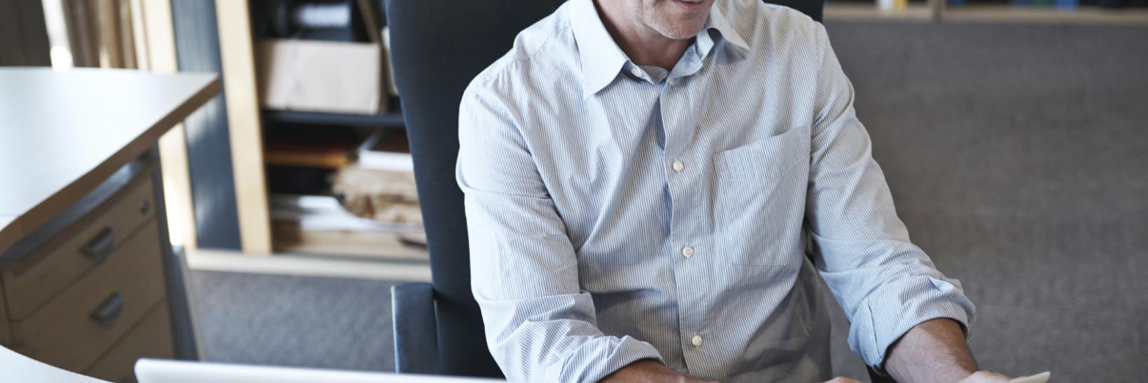 Man sitting at desk in front of a lap top, using his tablet