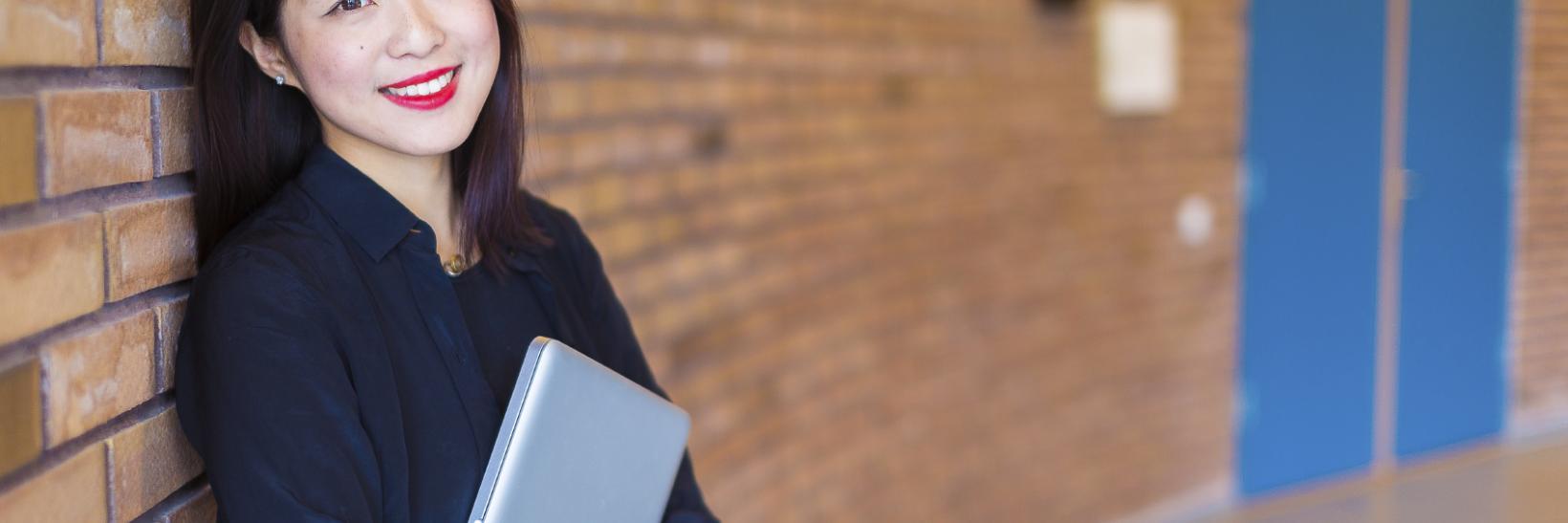 South Korean college student stands in a hallway with her laptop. 