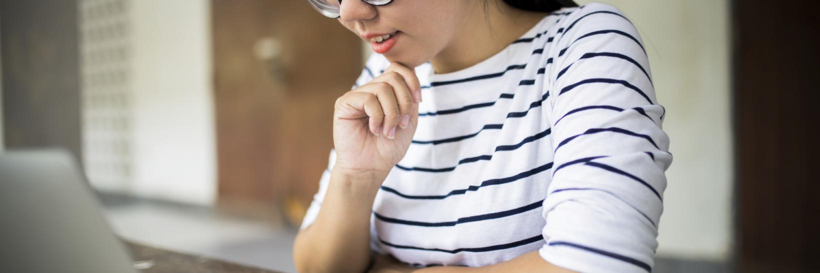 Young woman sitting at a table in front of a silver laptop. 