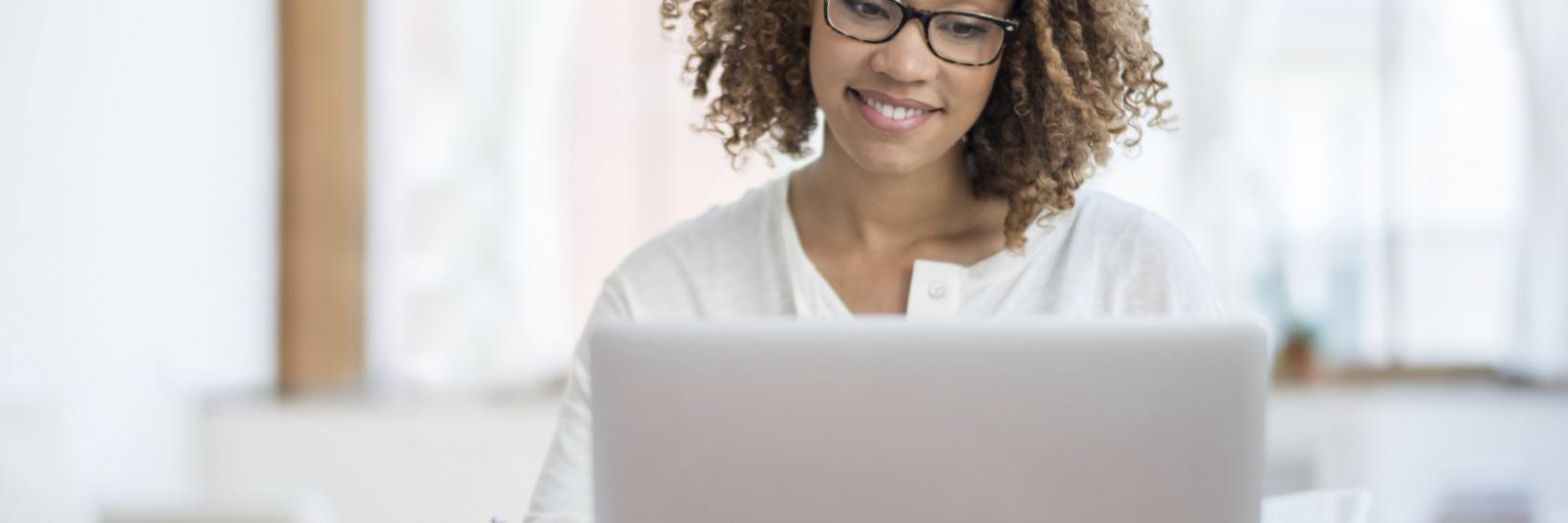 Young woman writing while looking at an open laptop computer