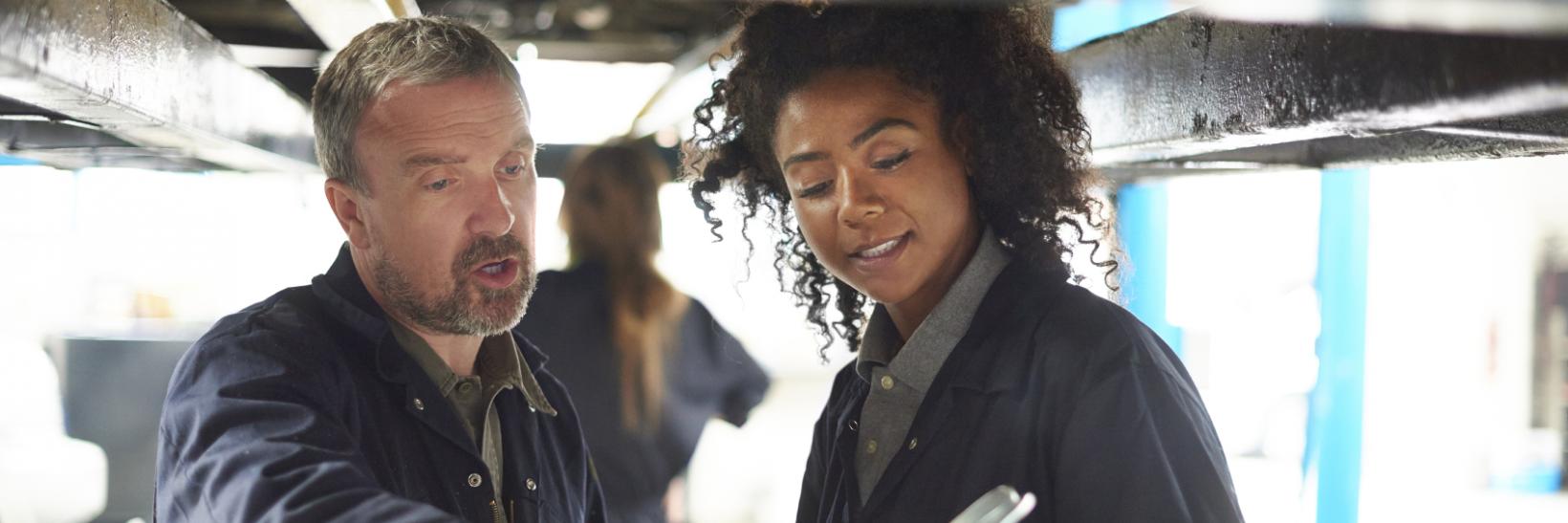 Female garage mechanic learning from her teacher. 