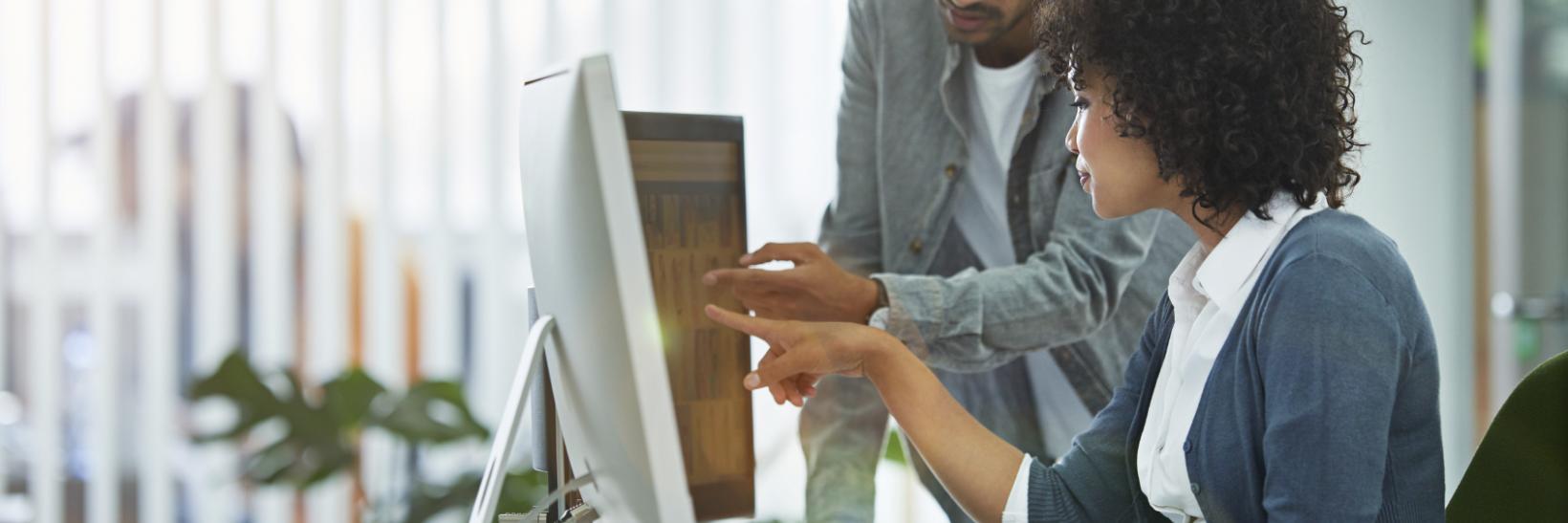 Man and woman looking at and pointing to two desktop computer monitors.