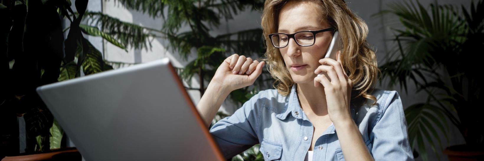 Woman sitting on an arm chair in front of a lap top, on her phone