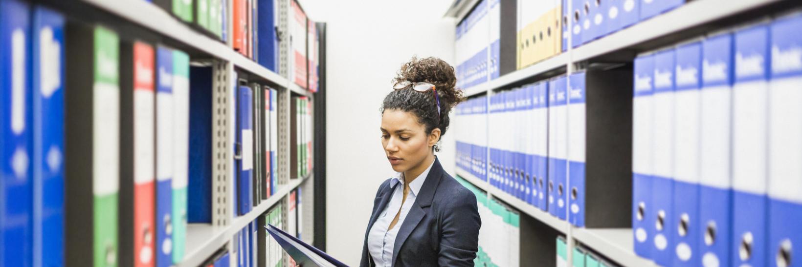 Young woman looks at binder while standing between two shelves