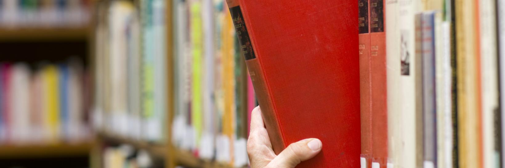 Student grabbing book from library shelf.