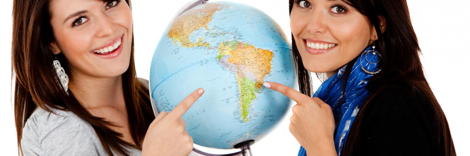 Female students pose next to globe. 