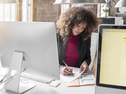 Woman sits at a desk with a computer and completes paperwork