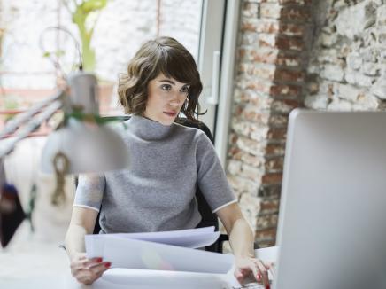 Woman sits at a computer at a desk and uses the new Frequently Asked Questions tool