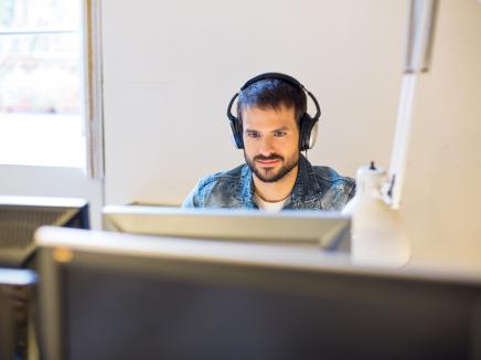 A stakeholder sits at a computer and listens to the Government Voices Webinar recording on headphones