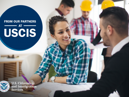 Two coworkers talking at a table, with the USCIS logo in the bottom right corner