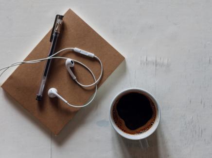 Coffee, a notepad, earphones and a pencil lying on an office desk.