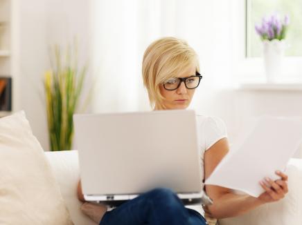 woman reads a form while on a laptop