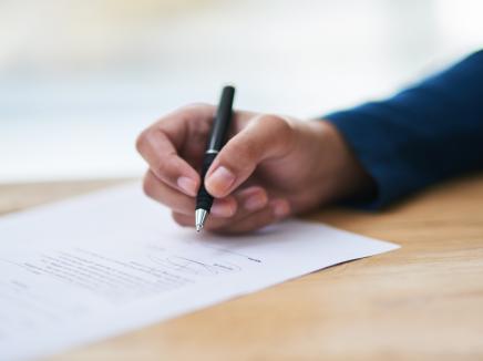 A hand writing on a piece of paper with a pen.