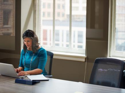 Woman sits and uses a laptop at a conference room table