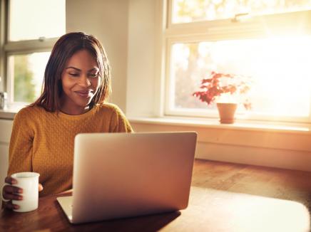 A woman drinking a coffee looking at her laptop computer.