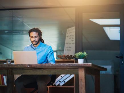 A man sitting a desk working on a laptop computer.