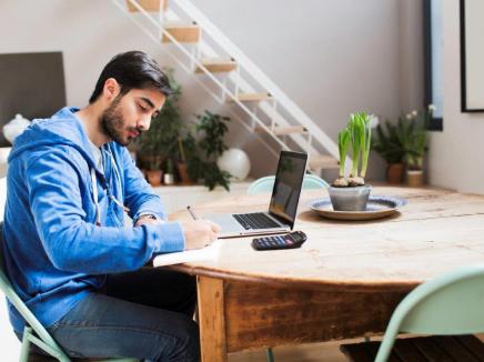 Young man sitting at a desk and writing in front of a computer