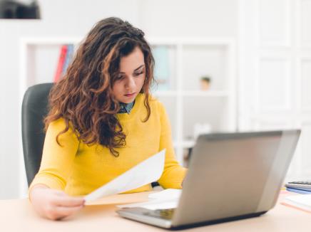 Businesswoman holding document and using laptop.