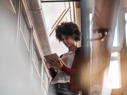 Young woman in the library standing beside the bookshelf and studying.