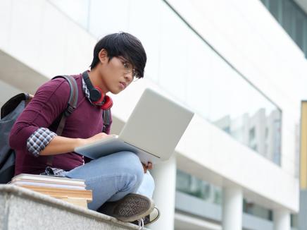 An international student working on his laptop outisde