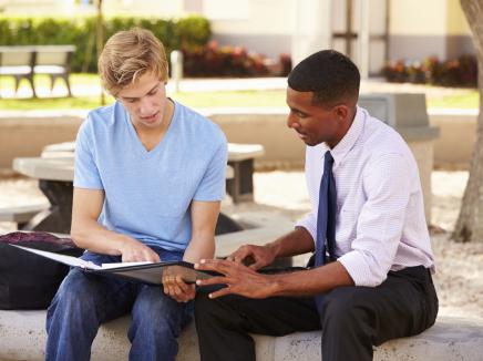Teacher sitting outdoors with a student. 