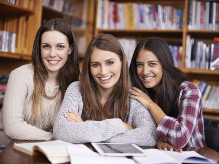Three female students smiling and studying at the library together
