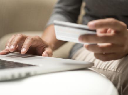 Close up of hands holding credit card in front of a laptop 