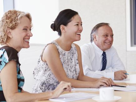 A man and two women sitting and smiling at a conference table. 