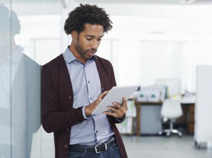 man leaning against a wall reading a tablet. 