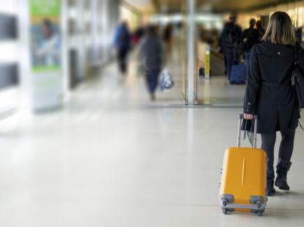 Woman walking in an airport with a roller bag suitcase 