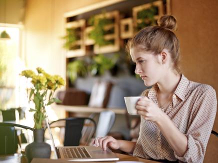 Woman drinking coffee working on a laptop 